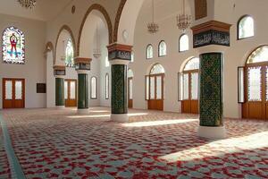 Sunlit mosque interior with patterned carpet, arches, and stained glass. photo