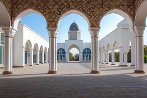 White mosque courtyard with arches, columns, and dome under a clear blue sky. photo