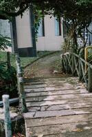 Old wooden bridge with rustic railings leading to a garden path, surrounded by lush greenery photo