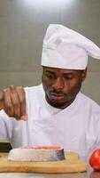 African American chef prepares salmon fillet on a wooden cutting board, process of sprinkling with spices and salt. Vertical video