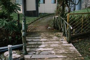 Old wooden bridge with rustic railings leading to a garden path, surrounded by lush greenery photo