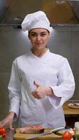 Portrait of smiling caucasian female chef with fresh salmon standing in hotel kitchen. Vertical video