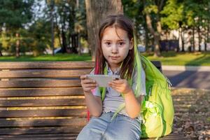 Girl on park bench using smartphone with backpack in autumn photo