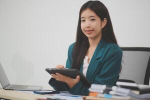 Beautiful Asian businesswoman work using a tablet and a laptop with documents placed at the office. photo