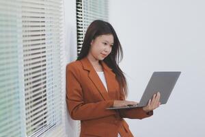 Attractive smiling Asian businesswoman standing holding tablet working and recording work details in office. photo