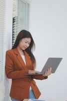 Attractive smiling Asian businesswoman standing holding tablet working and recording work details in office. photo