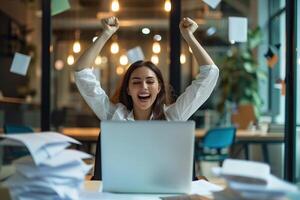 Happy excited young Hispanic business woman accountant standing at the desk working on laptop computer with a pile of documents on table in office and making yes gesture rejoicing in successful job. photo