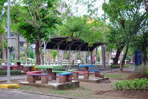 a vibrant garden setting featuring colorful picnic tables in the shade surrounded by lush greenery and shady trees. photo