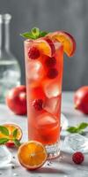 Refreshing summer drink with raspberries and citrus fruits in a tall glass on a marble countertop photo