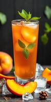Refreshing peach iced tea in a tall glass garnished with mint leaves surrounded by fresh peaches and ice cubes photo