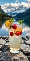 Refreshing drink with lemons and raspberries set against a picturesque mountain lake photo