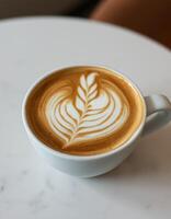 Latte art featuring a heart and leaf design in a white ceramic cup on a marble tabletop photo