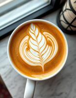 Coffee cup with intricate latte art placed on a marble table near a window, capturing morning light and warmth photo
