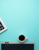 Workspace setup featuring a laptop, keyboard, and a cup of coffee on a vibrant blue desk photo