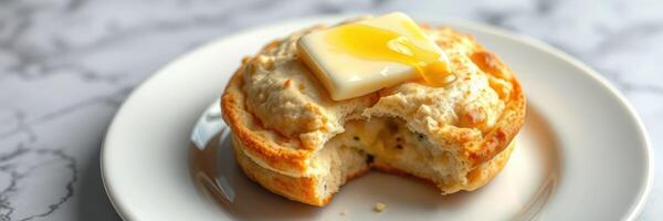 Freshly baked biscuit topped with melting butter on a white plate at a cozy breakfast table photo
