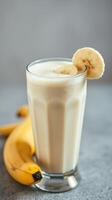 Creamy banana smoothie served in a tall glass with fresh banana slices on the rim beside ripe bananas photo