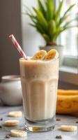Delicious banana smoothie served in a tall glass with a pink striped straw and fresh banana slices photo