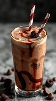 Creamy chocolate beverage topped with syrup and berries served in a tall glass with striped straws photo