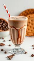 Chocolate milkshake with swirls of caramel served in a tall glass with a straw and surrounded by chocolate treats photo