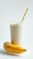 Creamy banana smoothie in a glass with a striped straw next to a fresh banana on a white background photo