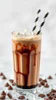 Delicious chocolate milkshake with ice and striped straws served in a tall glass on a white backdrop photo