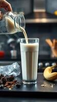 Pouring milk into a tall glass alongside coffee beans and a banana in a cozy kitchen setting photo