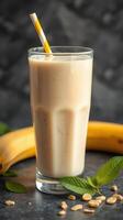 Creamy banana smoothie with oats and mint leaves garnished with a yellow straw on a dark countertop photo