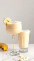Creamy banana smoothie served in a stylish glass along with a refreshing beverage on a marble countertop photo