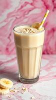 Creamy banana oat smoothie served in a tall glass with a striped straw on a pink marbled background photo