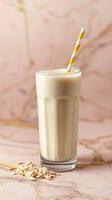 Creamy oat milkshake topped with a striped straw placed on a marble surface with oats beside it photo