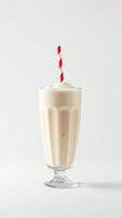 Creamy milkshake served in a classic glass with a red and white striped straw against a plain background photo