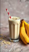 Creamy banana smoothie with oats served in a glass next to fresh ripe bananas on a marble surface photo