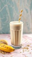 Creamy banana smoothie served in a tall glass with a striped straw and oats beside it on a pink surface photo