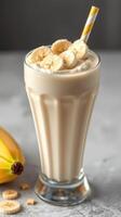 Creamy banana smoothie topped with fresh banana slices in a tall glass with a straw photo