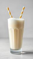 Creamy milkshake served in a glass with yellow striped straws and a simple background photo