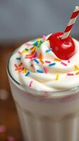 Creamy milkshake topped with whipped cream, sprinkles, and a cherry served in a tall glass photo