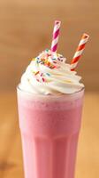 Delicious pink milkshake topped with whipped cream and colorful sprinkles in a glass with striped straws photo