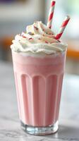 Creamy pink milkshake topped with whipped cream and colorful sprinkles in a tall glass with striped straws photo