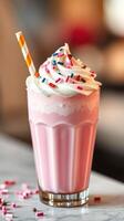 Delicious pink milkshake topped with whipped cream and colorful sprinkles in a glass on a countertop photo