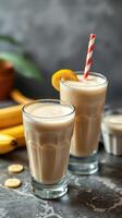 Delicious creamy banana smoothies served in glasses with striped straws and fresh fruit on a marble countertop photo