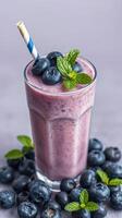 Smoothie prepared with fresh blueberries and mint served in a tall glass with a striped straw photo