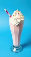 Creamy milkshake topped with whipped cream and colorful sprinkles served in a tall glass against a vibrant blue backdrop photo
