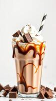 Delicious chocolate caramel milkshake topped with whipped cream and chocolate pieces in a clear glass photo
