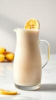 Refreshing lemon smoothie served in a glass pitcher with lemon slice on top and fruit in background photo
