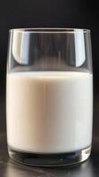 Close up of a glass filled with fresh milk against a dark background in a well-lit setting photo