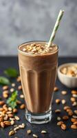 Delicious peanut butter smoothie topped with crushed nuts served in a tall glass on a dark background photo