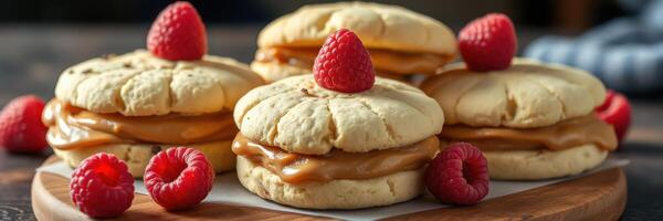 Delicious cookies filled with caramel and topped with fresh raspberries on a wooden platter photo