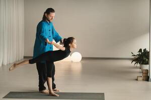 A yoga instructor in training helps a child to do exercises in the gym photo