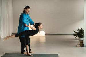 A yoga instructor in training helps a child to do exercises in the gym photo