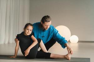 A yoga instructor in training helps a child to do exercises in the gym photo